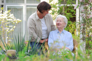 Foto einer ehrenamtlichen Helferin mit einer Bewohnerin im Garten. 